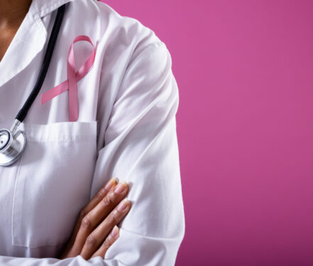 Midsection of african american mid adult doctor with pink breast cancer awareness ribbon, copy space. pink background, doctor, medical, awareness, support, healthcare and medical occupation.
